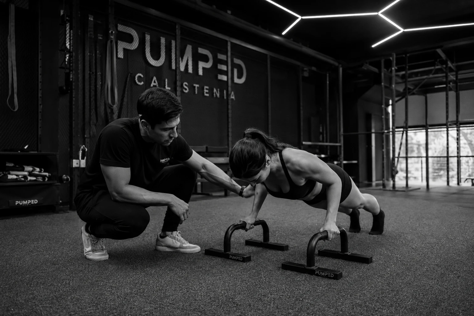 Coach de Pumped guiando a una socia en lagartijas sobre paraletas — entrenamiento personal 1 a 1 en Guadalajara